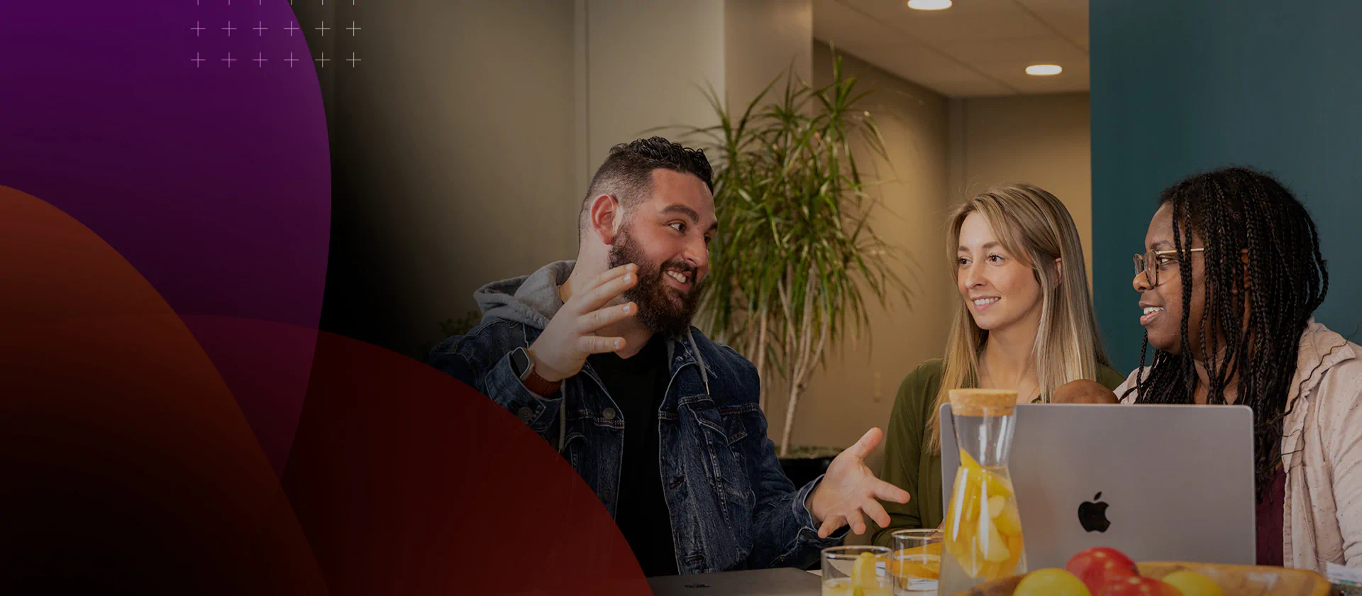 Three people talking around a laptop in an image published on MIM’s careers website