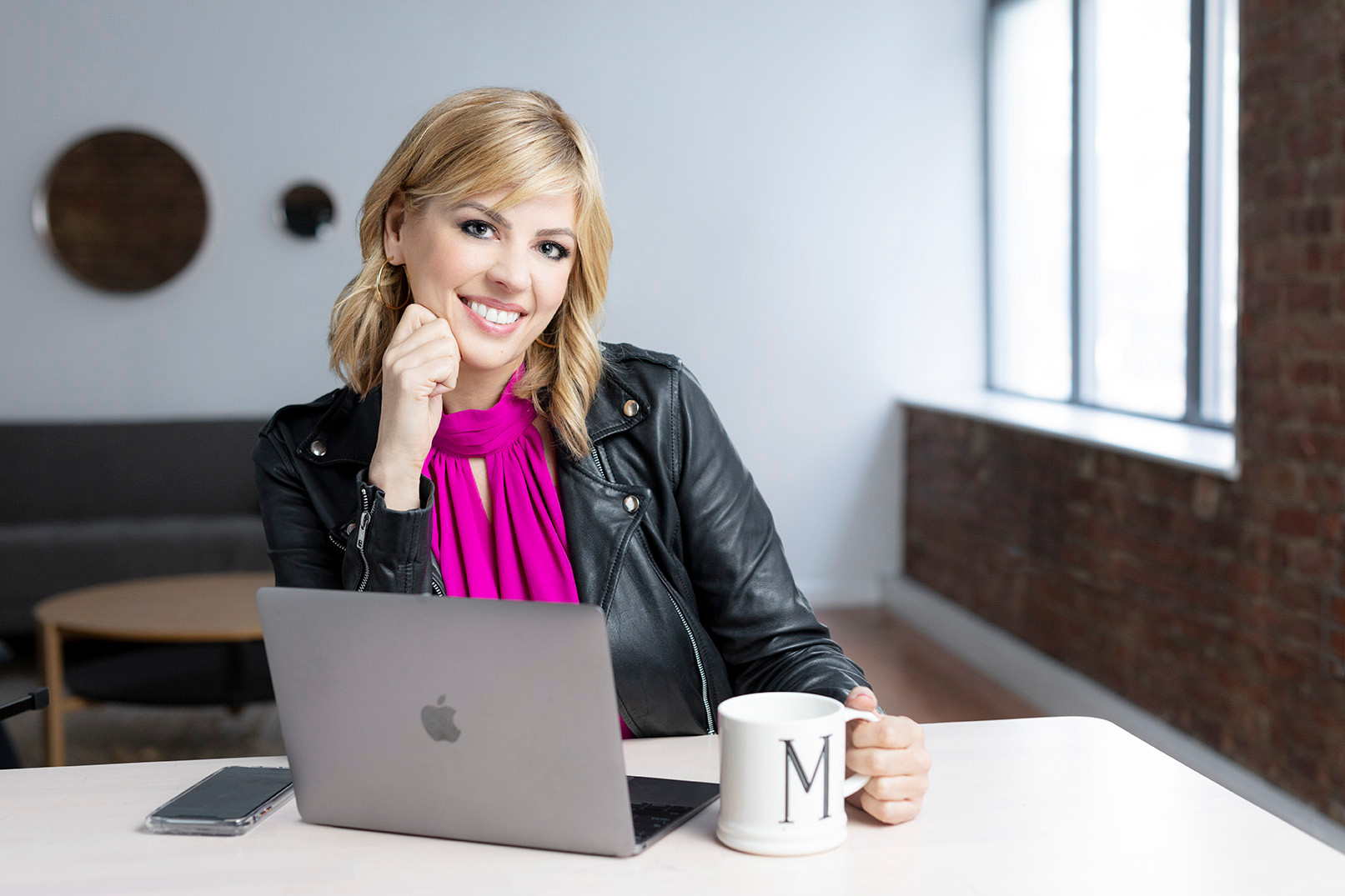 Mimi Banks seated at a desk with a laptop and a mug bearing the letter M