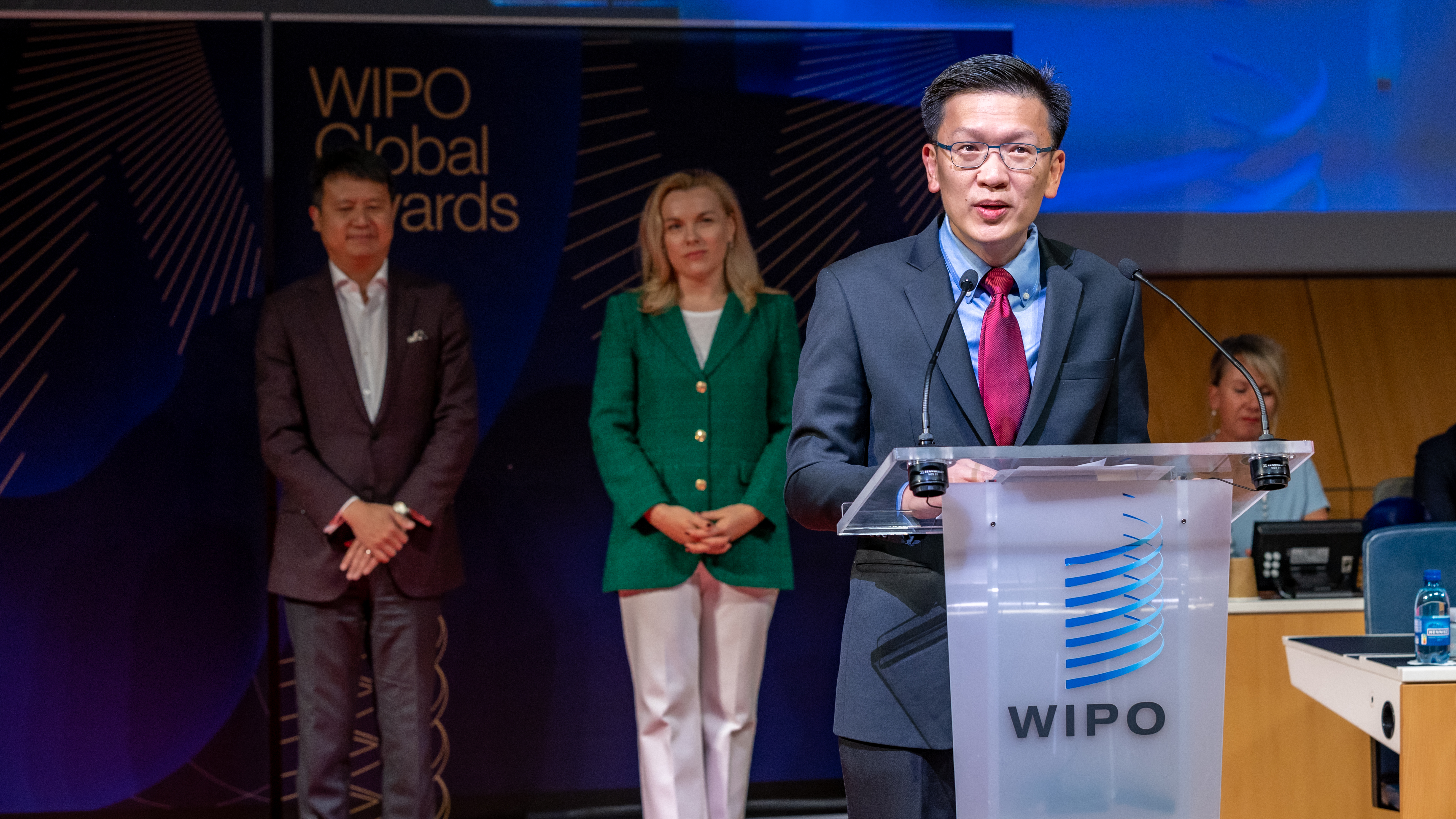 Min-Han Tan speaking at a transparent lectern at the 2022 WIPO Global Awards, with Daren Tang and Tatiana Molcean behind him.