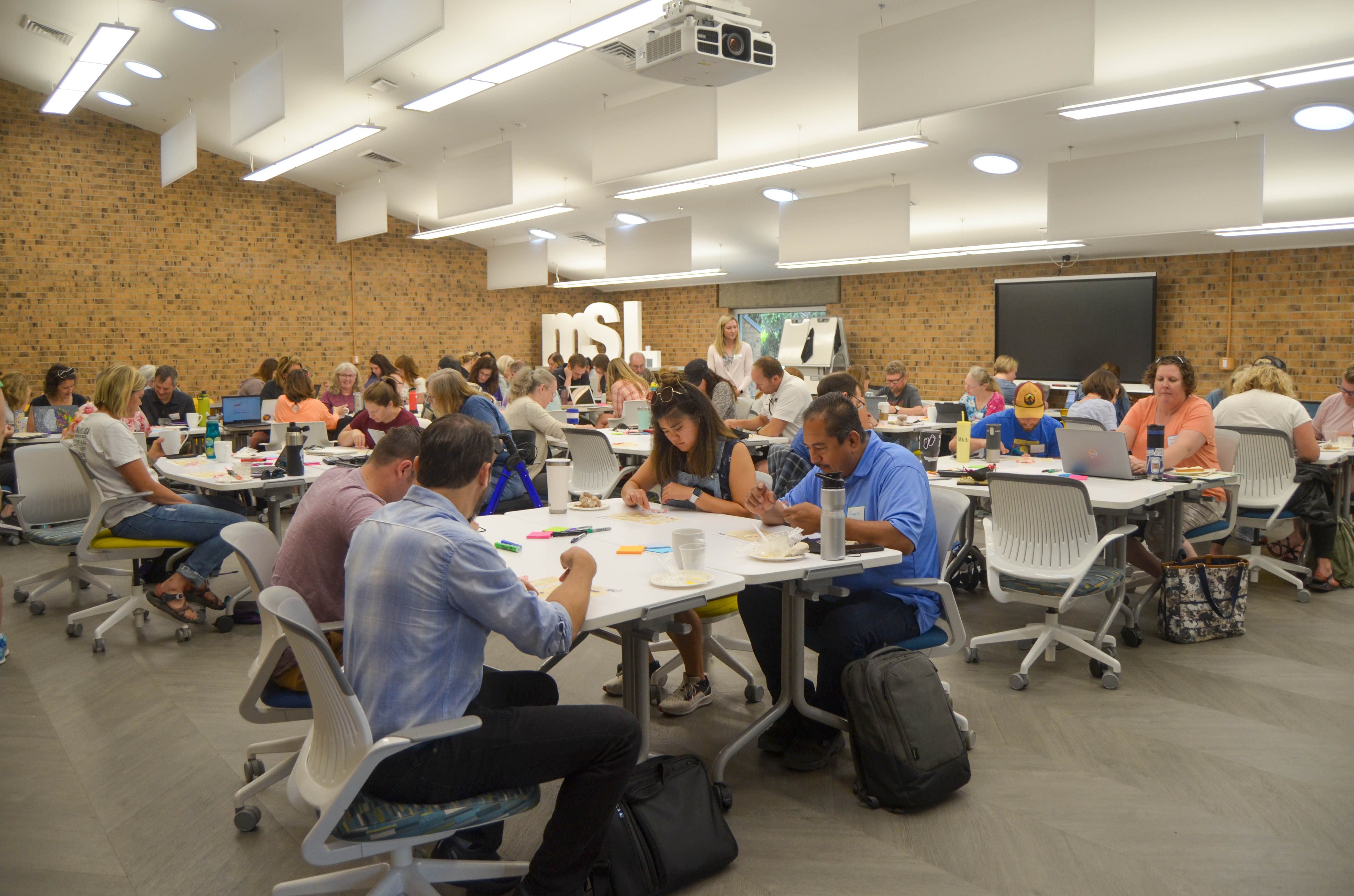 Educators seated around tables collaborating during a MindSpark professional learning session