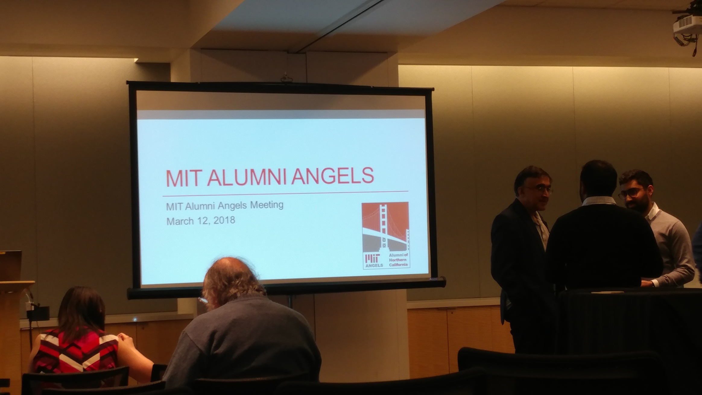 Attendees talking beside the MIT Alumni Angels presentation screen at the March 12, 2018 meeting