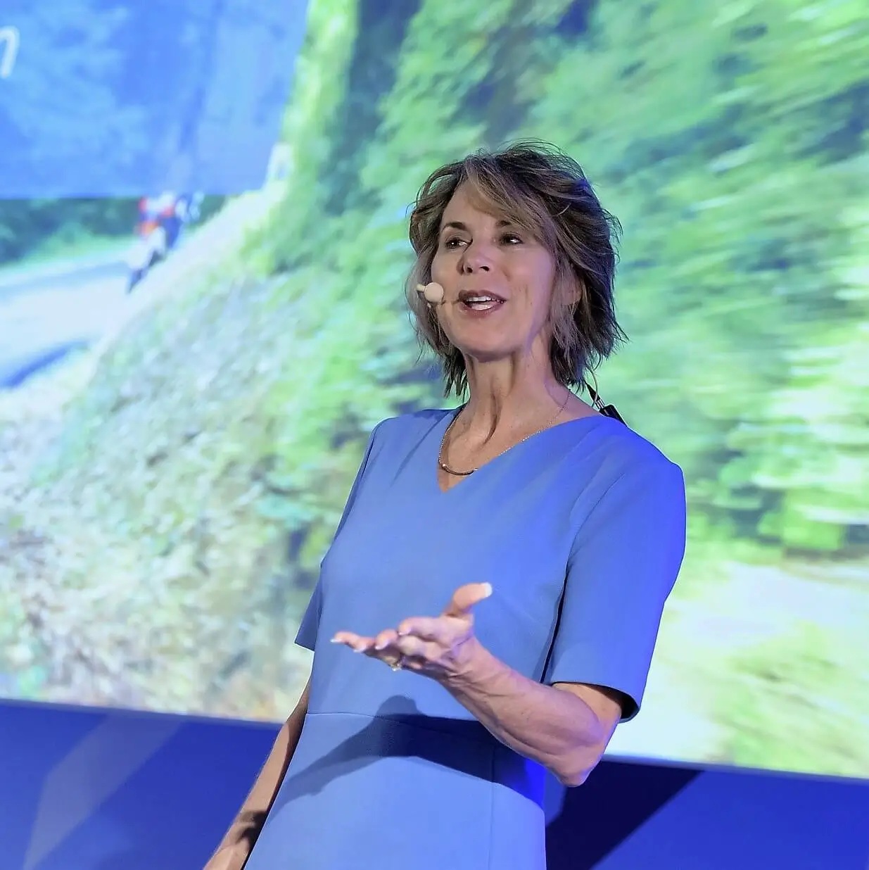 Elise Mitchell speaking onstage, with an image of a winding road behind her