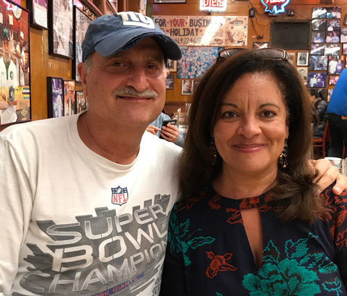 Mitchell Trager wearing a New York Giants cap beside a companion in a restaurant