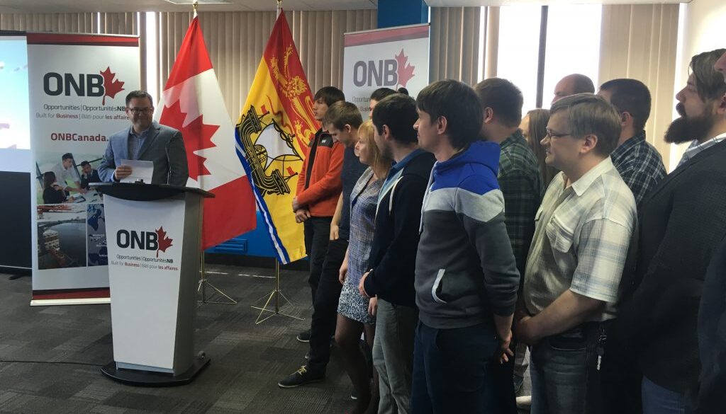 Mitchell Weisman at a lectern alongside members of RevJet’s relocated team in Saint John