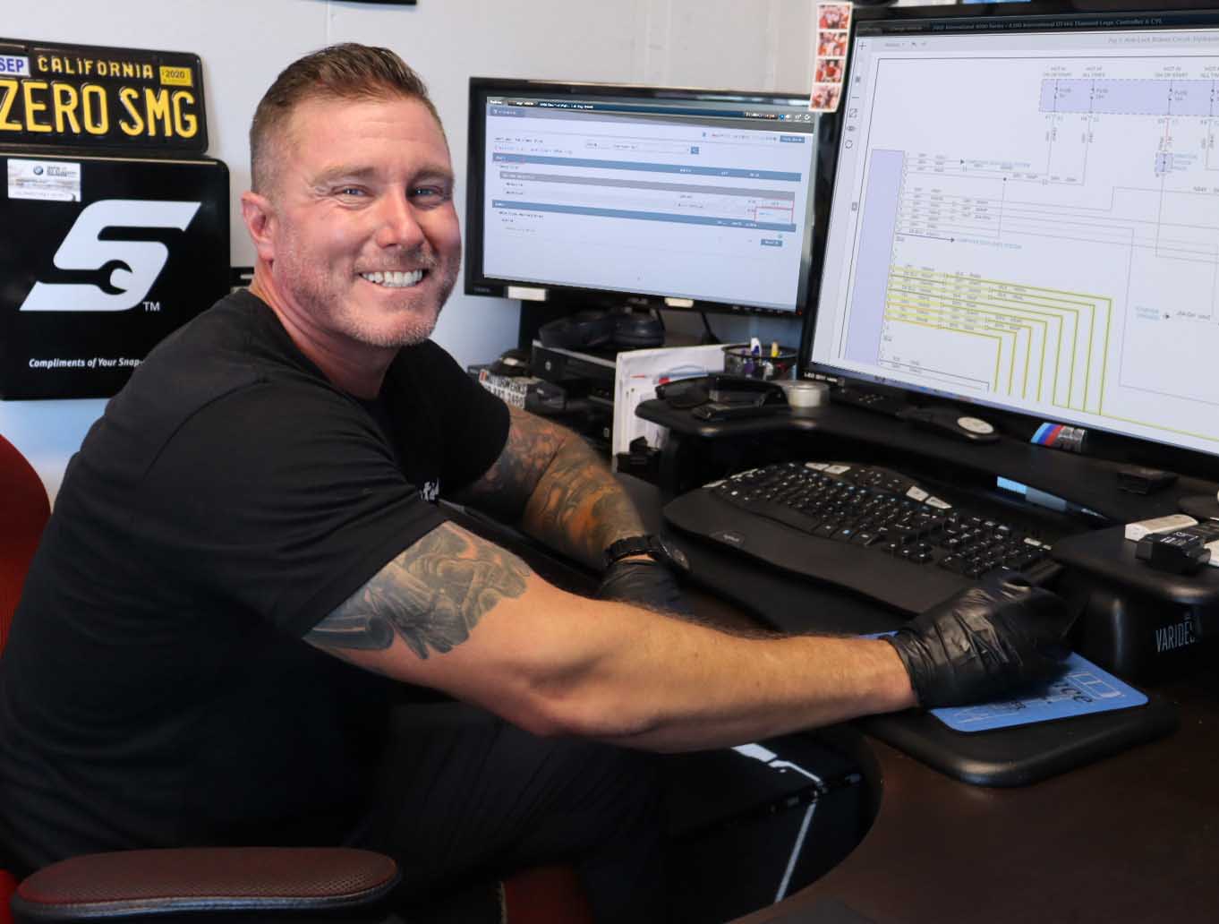 Technician at a shop computer with repair information and a wiring diagram on two screens