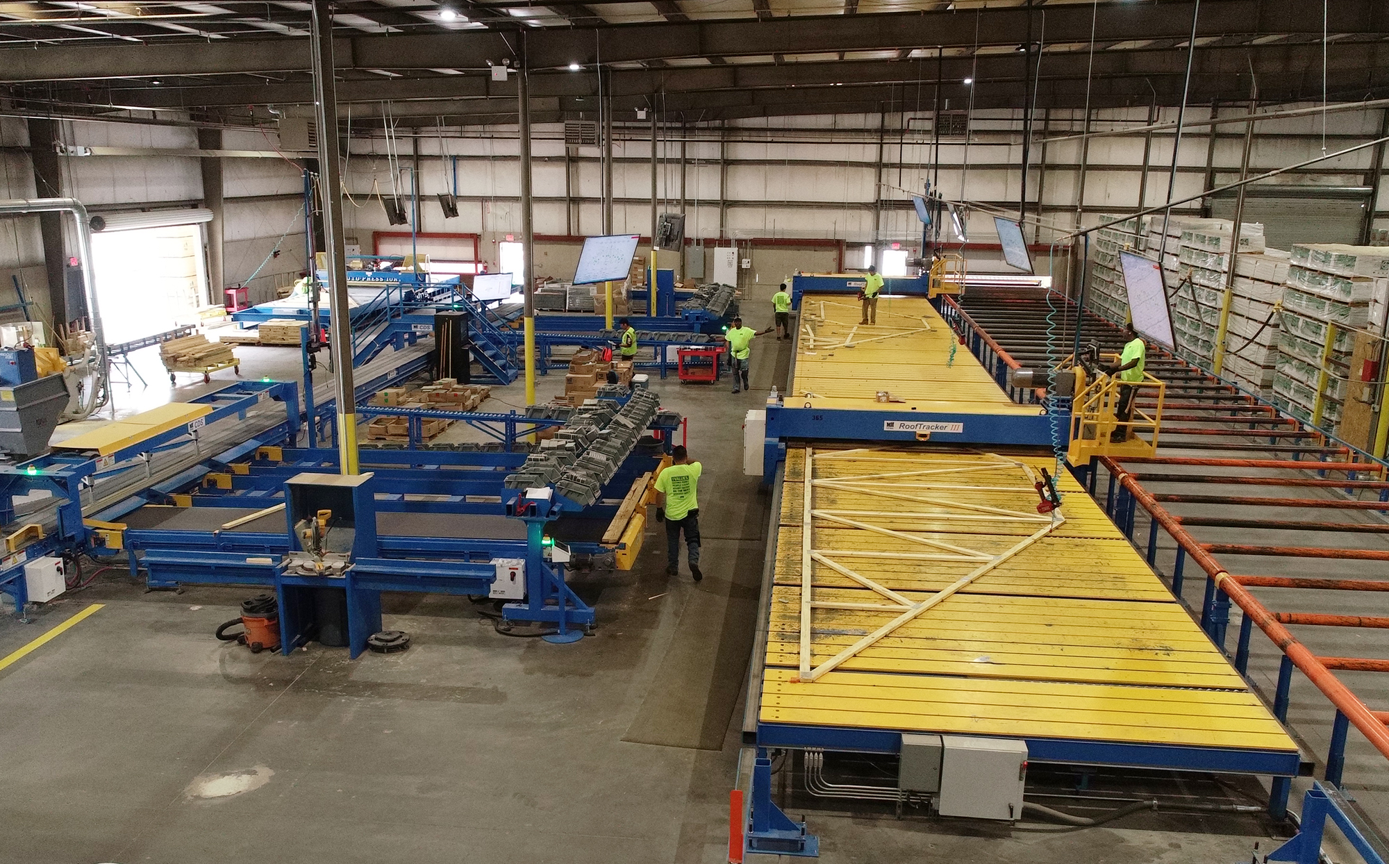 Automated equipment handling a wooden roof truss inside a component manufacturing facility