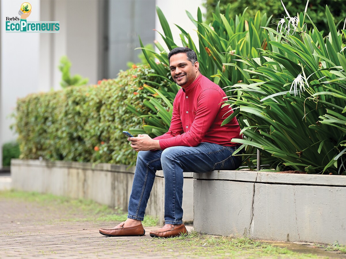 Mithun Suvarna seated beside a planted terrace, wearing a red shirt