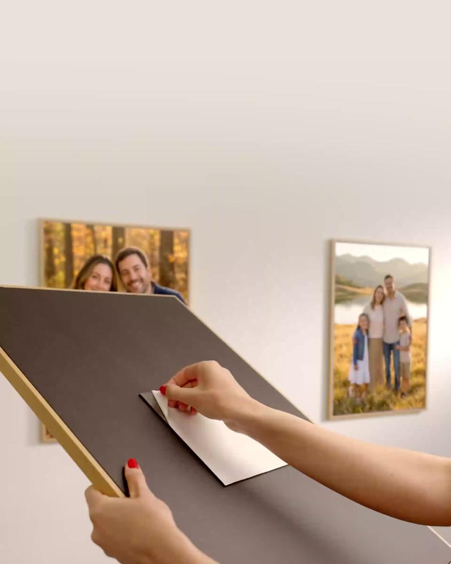 A person peels the backing from a Mixtiles frame, with family photographs already hanging behind it