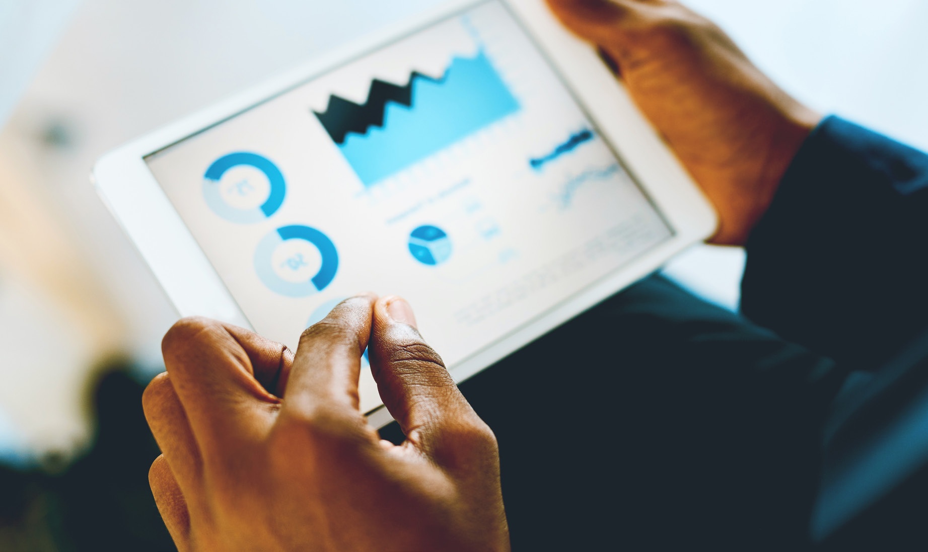 Illustrative photograph of someone reviewing blue analytics charts on a tablet