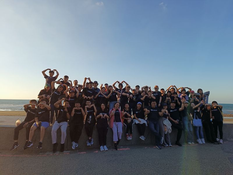 MoBagel team members gathered beside the sea, many making heart shapes with their arms