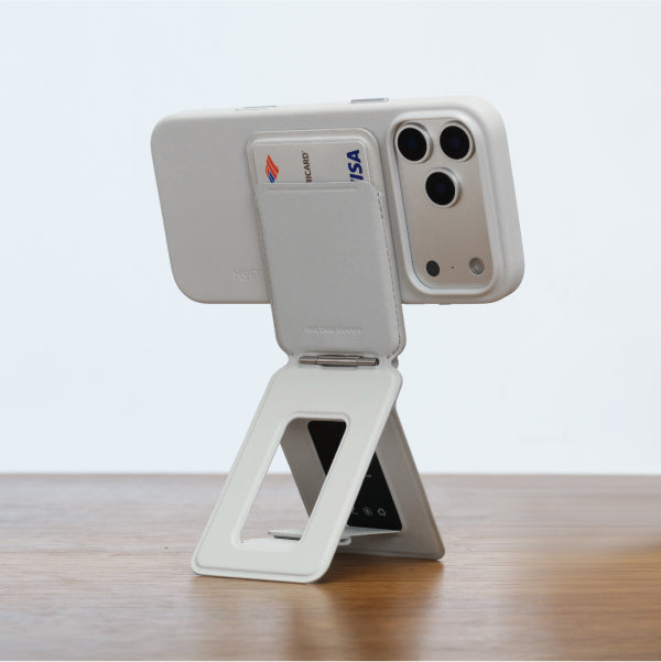 A phone propped up on MOFT's folding MagSafe wallet-stand with cards beside it