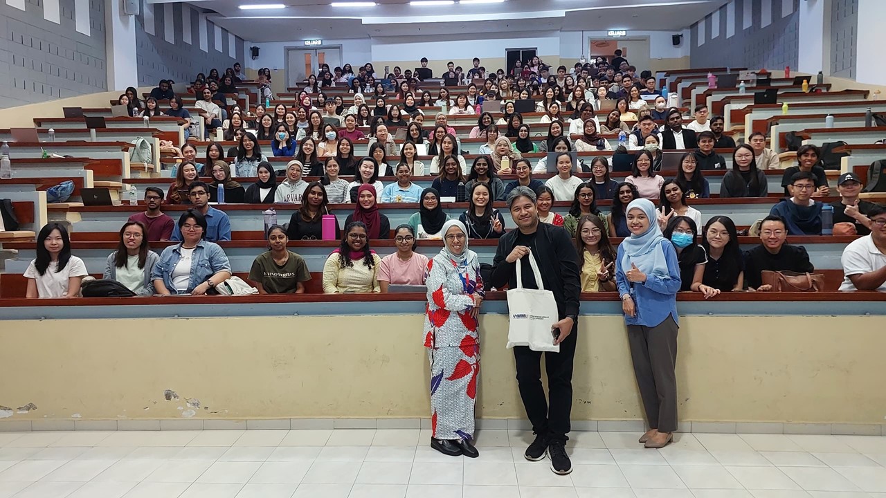 Iskandar standing with students and university representatives in a tiered lecture hall at MMU Melaka