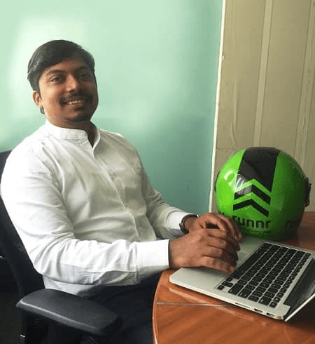Mohit Kumar seated at a laptop beside a bright green Runnr delivery helmet