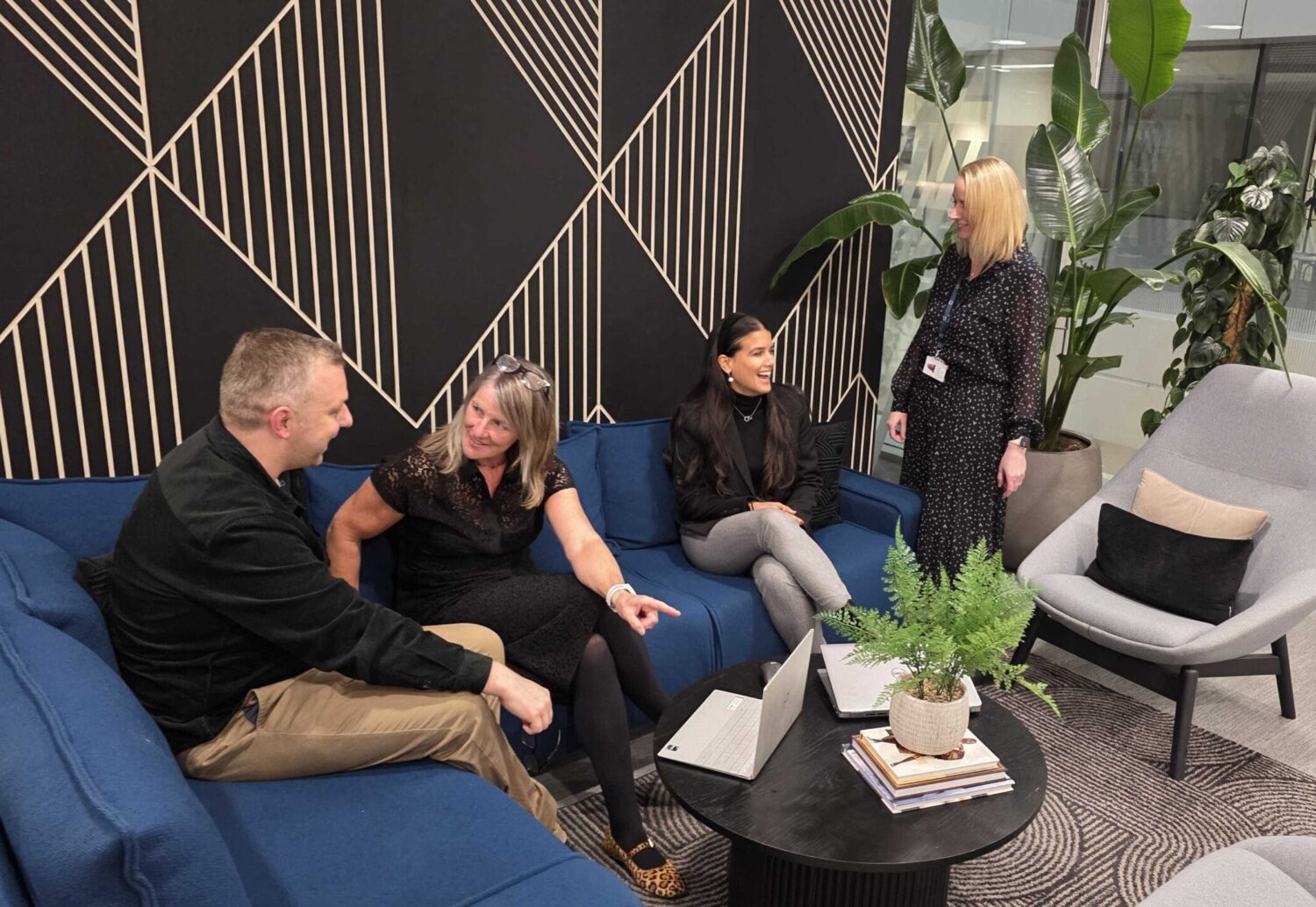 Four people talking around laptops in Moneyhub’s published team photograph
