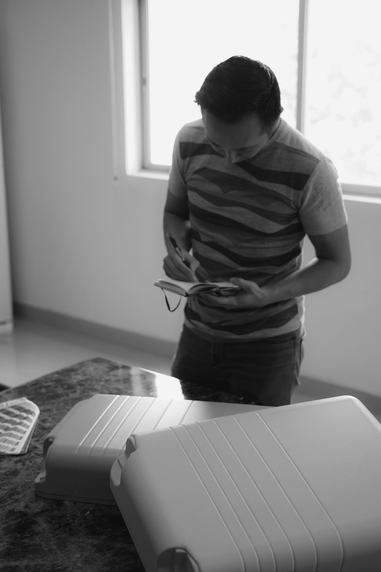A Monos design-process photograph showing a man examining suitcase shells at a table