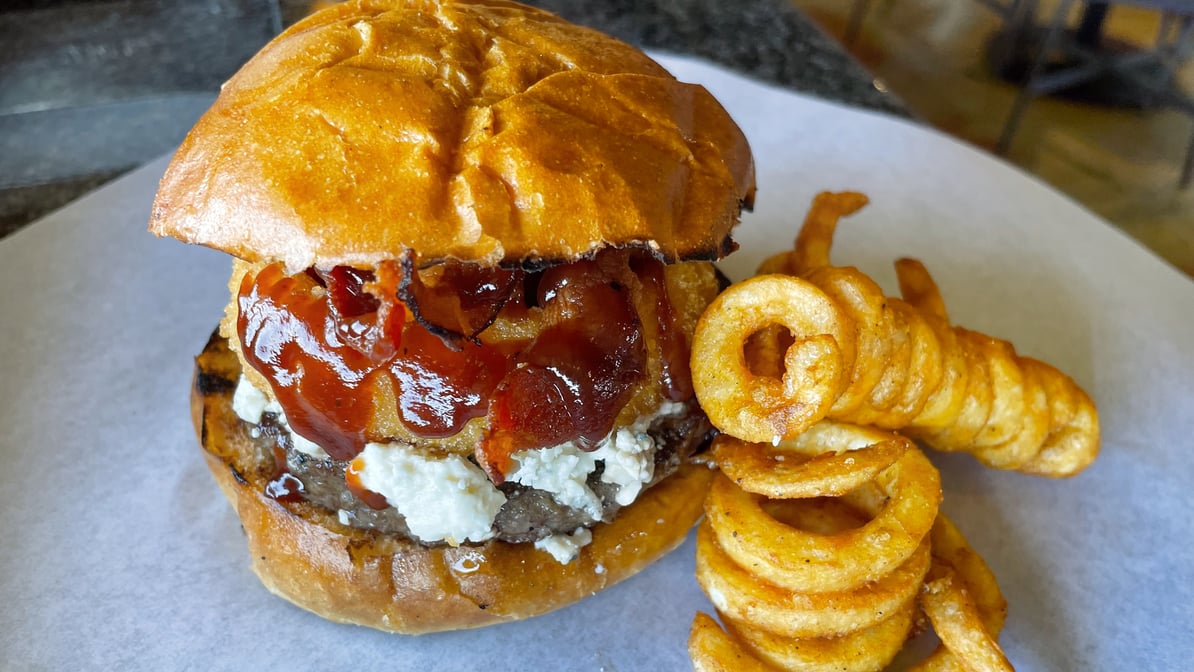 A Monsoon Burger with bacon, barbecue sauce and curly fries on a white plate