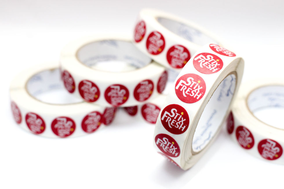 Rolls of red and white StixFresh fruit stickers on a white surface