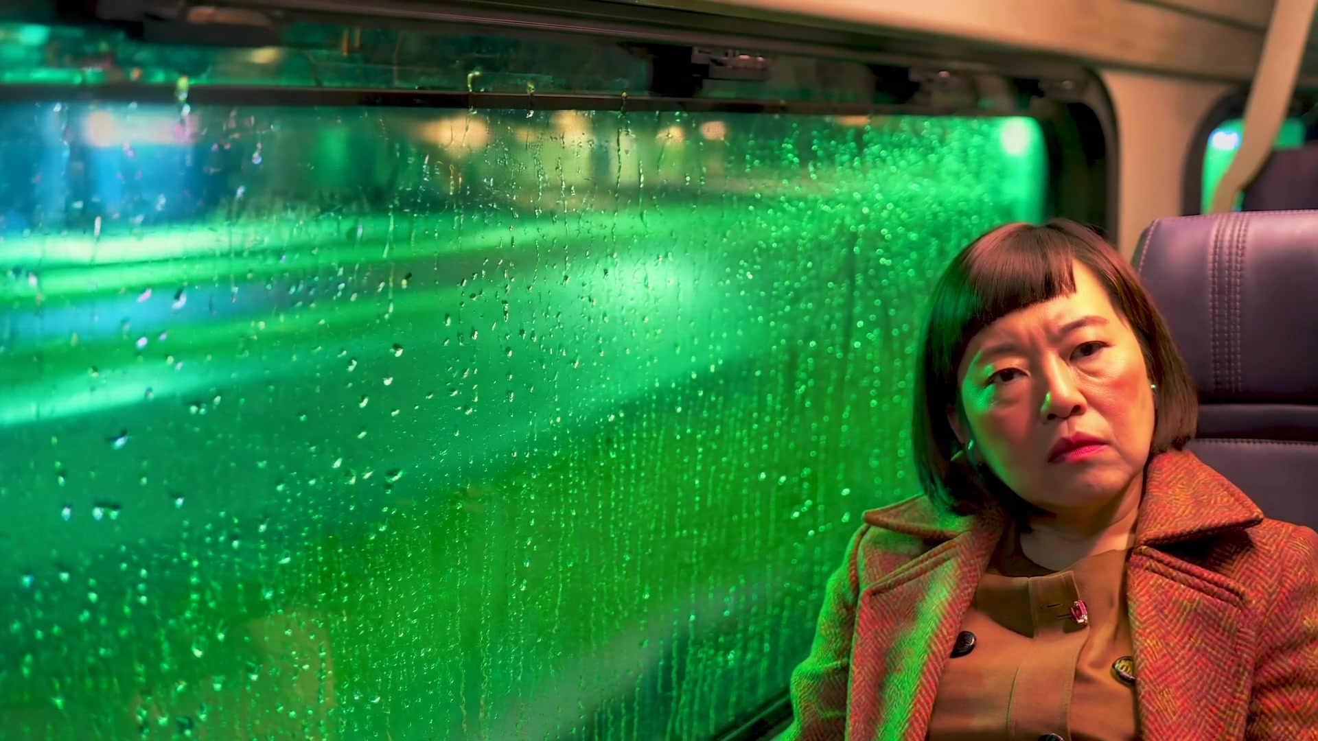 A woman sitting beside a rain-covered green train window in a Moonvalley Marey demonstration