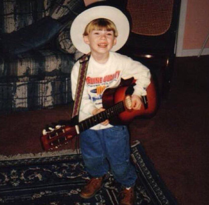 Morgan Wallen as a young child wearing a cowboy hat and holding a guitar