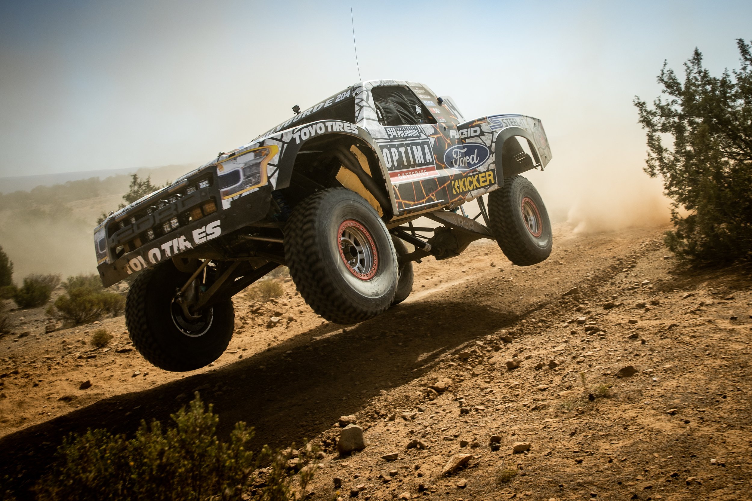 An OPTIMA-sponsored off-road racing truck airborne over a desert trail