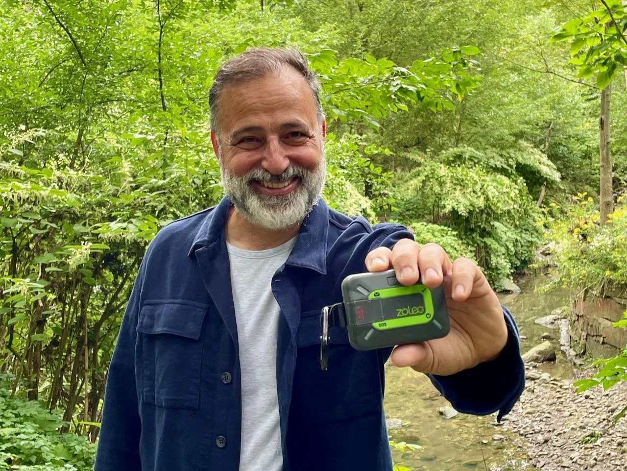 Morris Shawn outdoors, holding a green-and-grey ZOLEO satellite communicator toward the camera