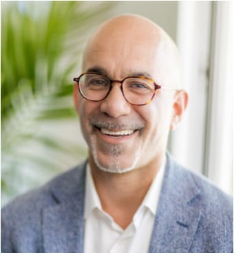 Moshe Pinto smiling in a blue jacket beside a window