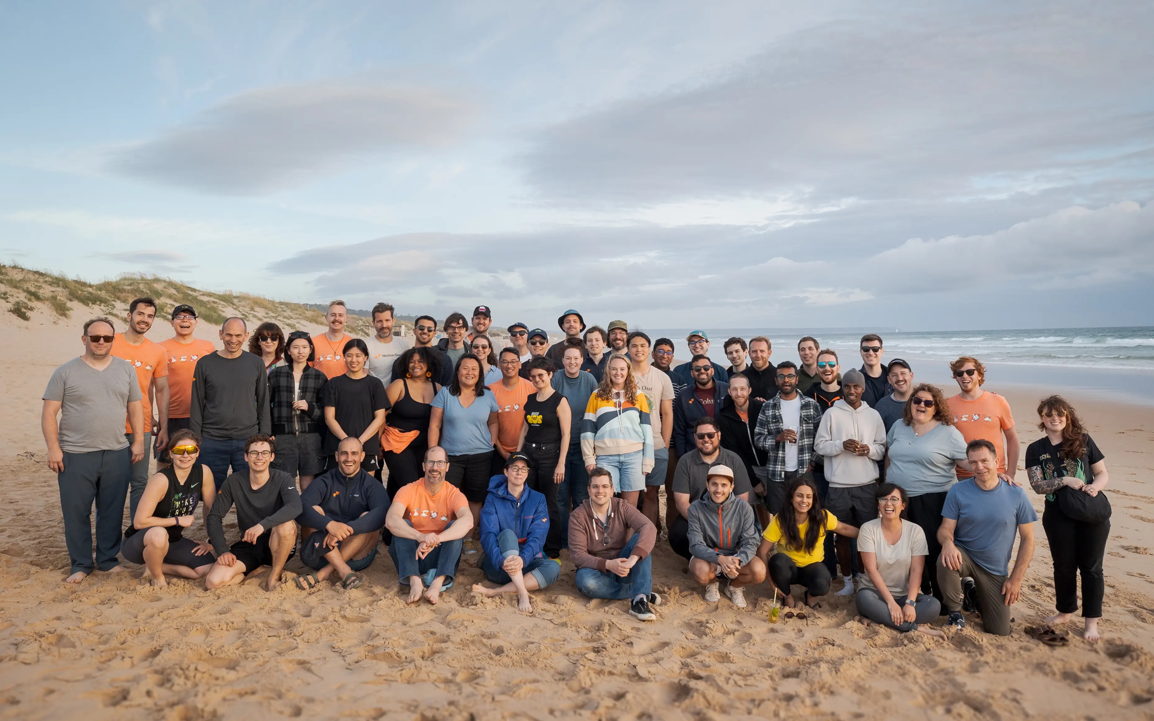 MotherDuck team gathered on a sandy beach beside the sea