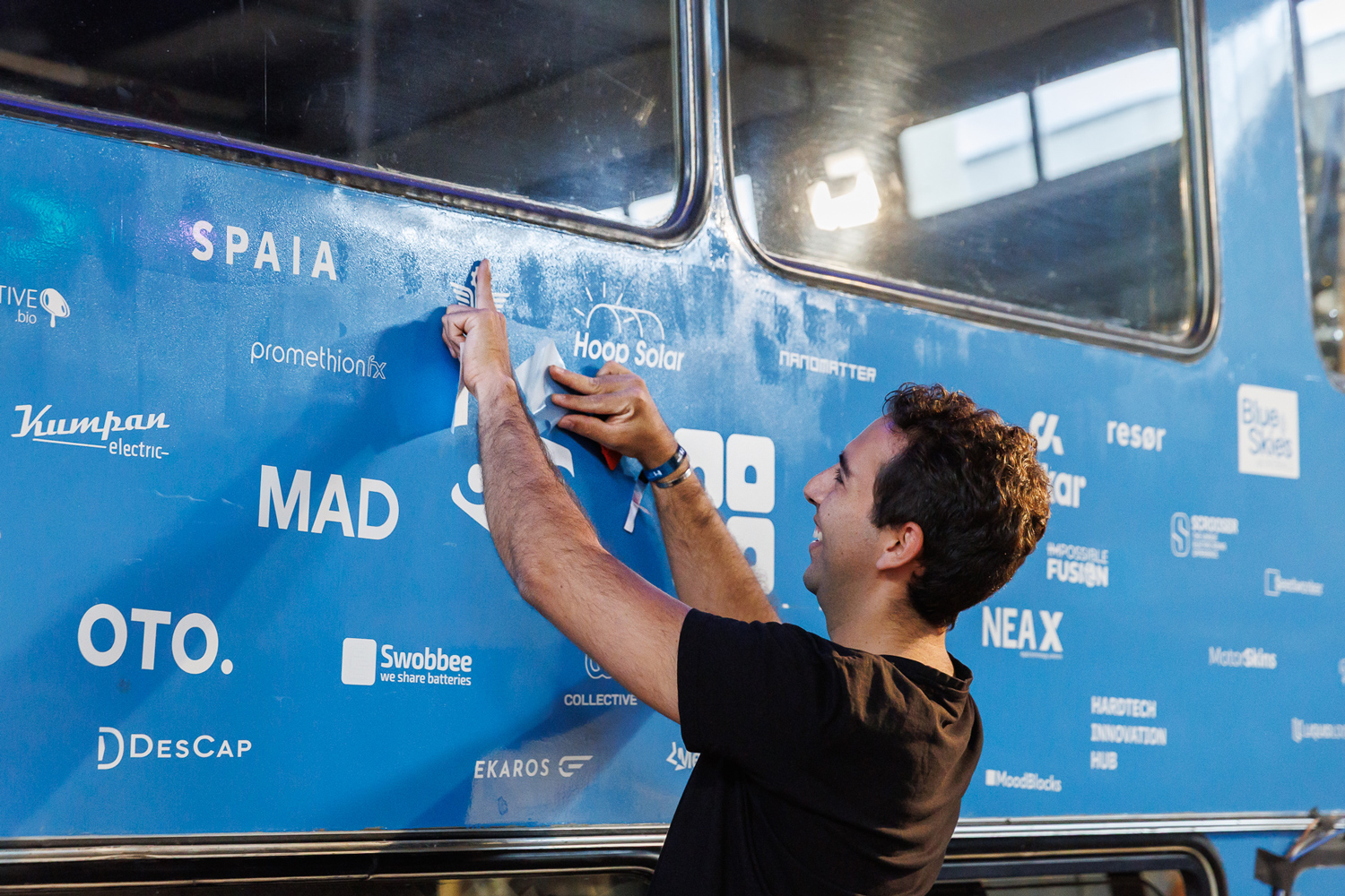 A person adding a company name to MotionLab.Berlin’s blue double-decker bus