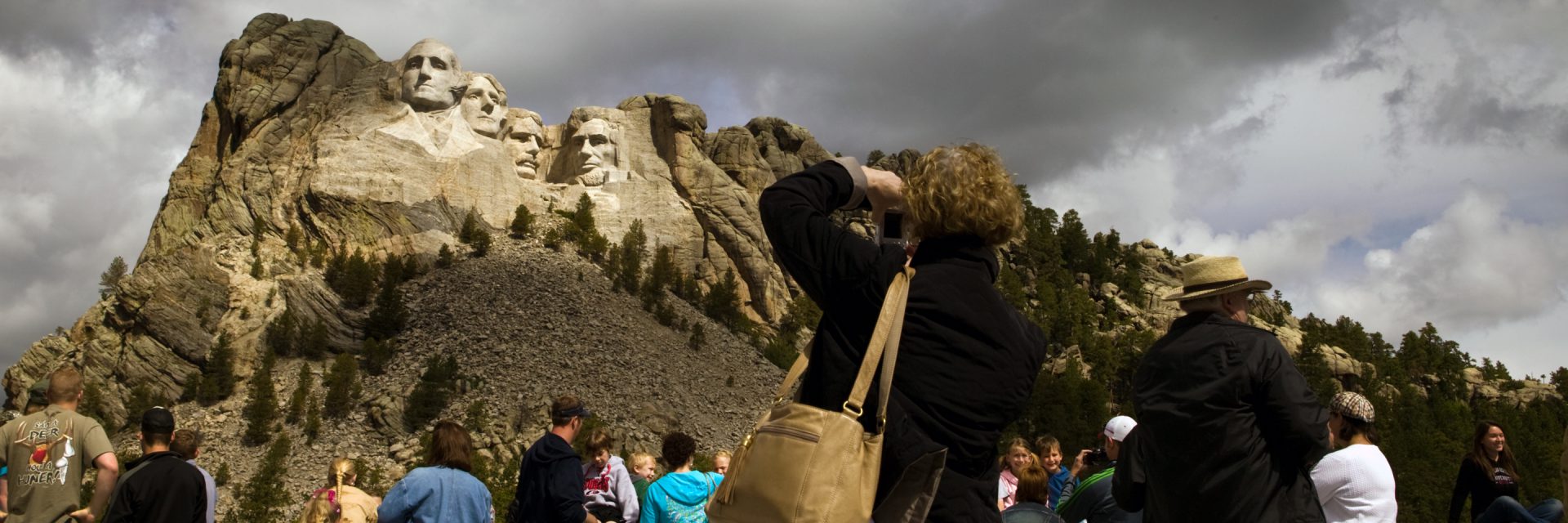 Visitors looking toward Mount Rushmore beneath a dramatic sky