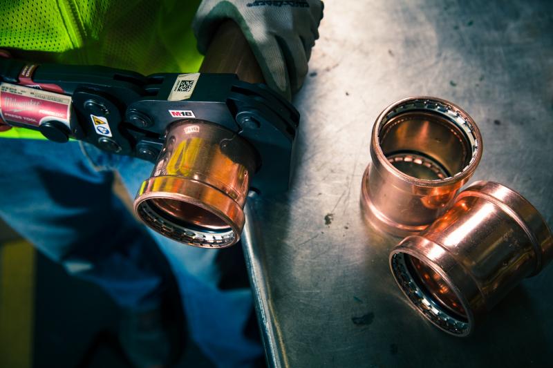 Copper press fittings beside a press tool on a metal workbench