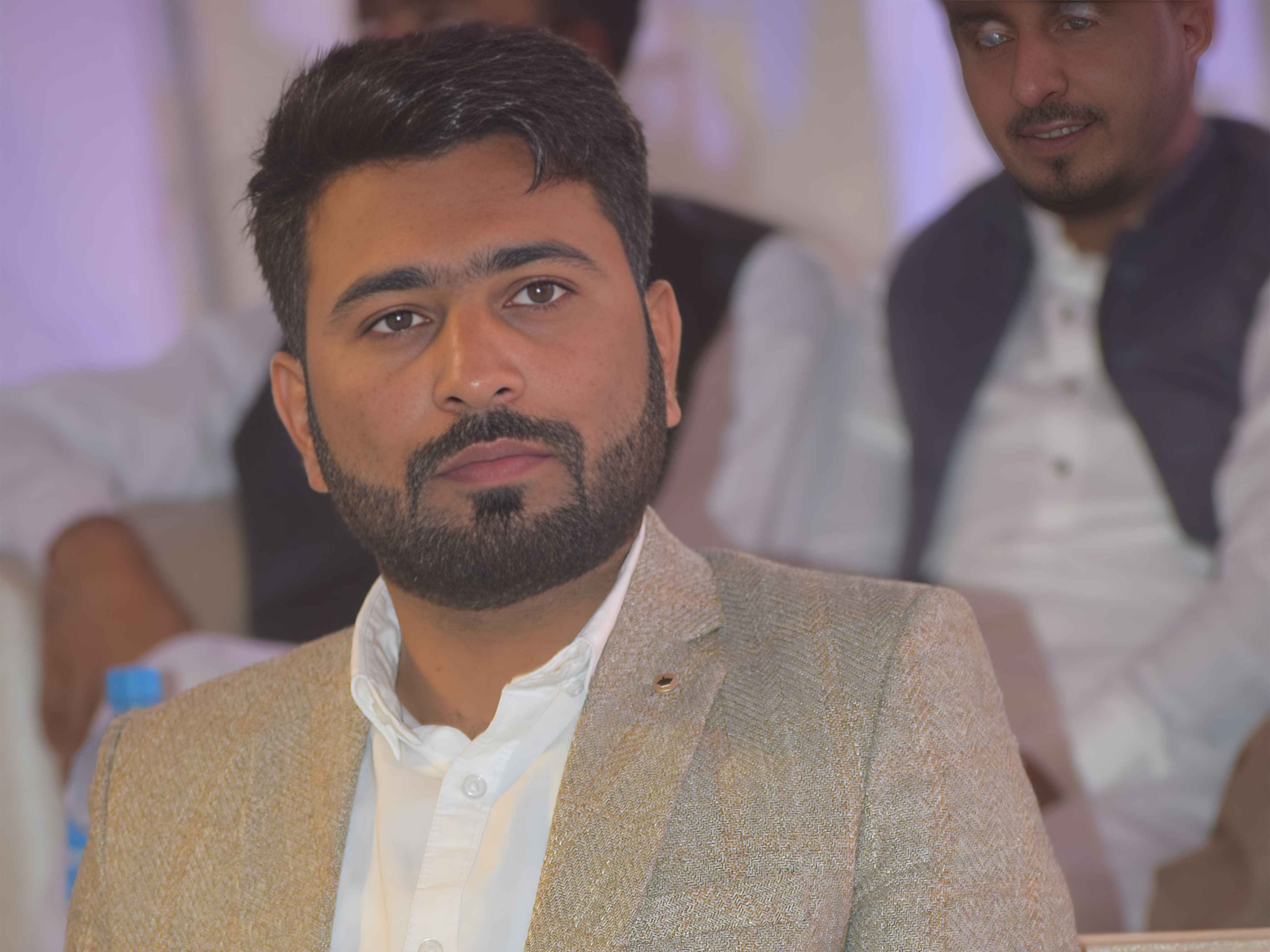Muhammad Imran seated at a Manisofts gathering, wearing a tan jacket and white shirt