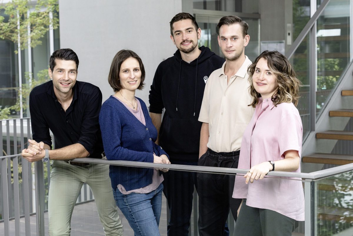 Five members of the Munich Startup team standing beside a railing in a bright building