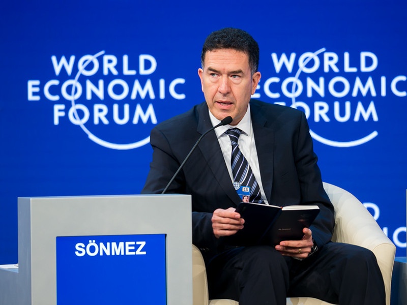 Murat Sonmez speaking at the World Economic Forum, with a notebook in his hands