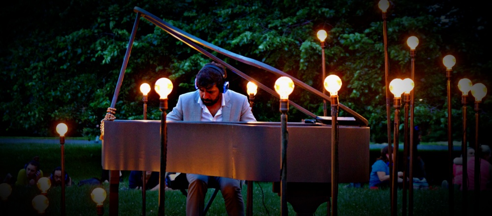 Murray Hidary plays an outdoor piano surrounded by glowing lamps and trees