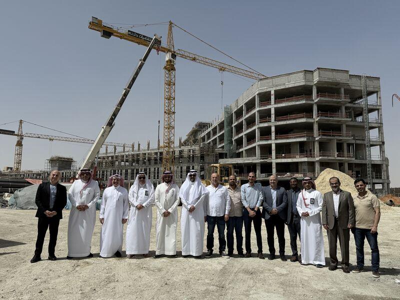 Colleagues stand in front of the concrete frame and cranes at Dallah’s Al-Arid construction project