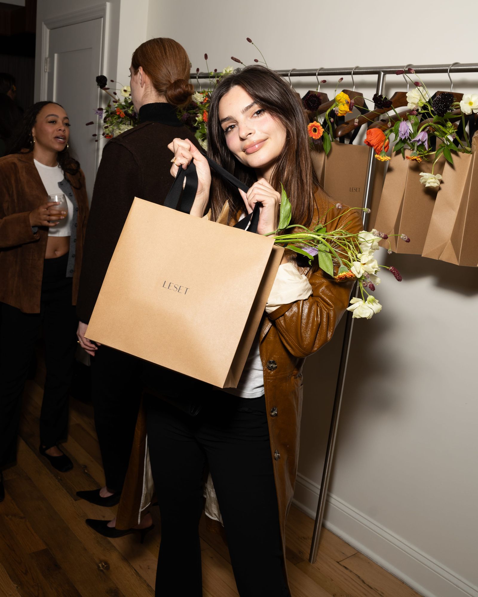 Emily Ratajkowski holding a Leset gift bag filled with flowers at a brand event