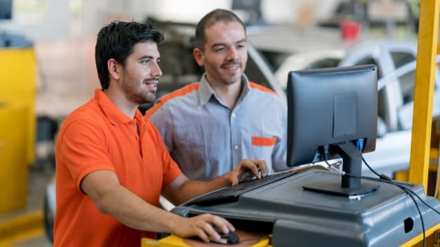 Two people collaborating at a computer inside an automotive repair shop