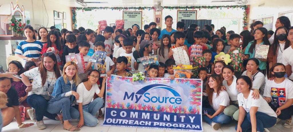 MySource community outreach gathering at the Lingap Center with wrapped gifts and a company banner