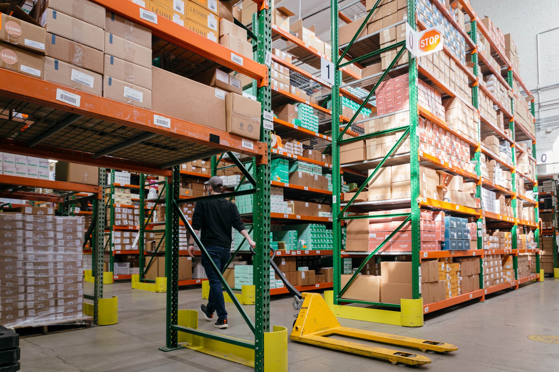 A warehouse worker moves a pallet jack between tall racks of boxed cannabis products at Nabis