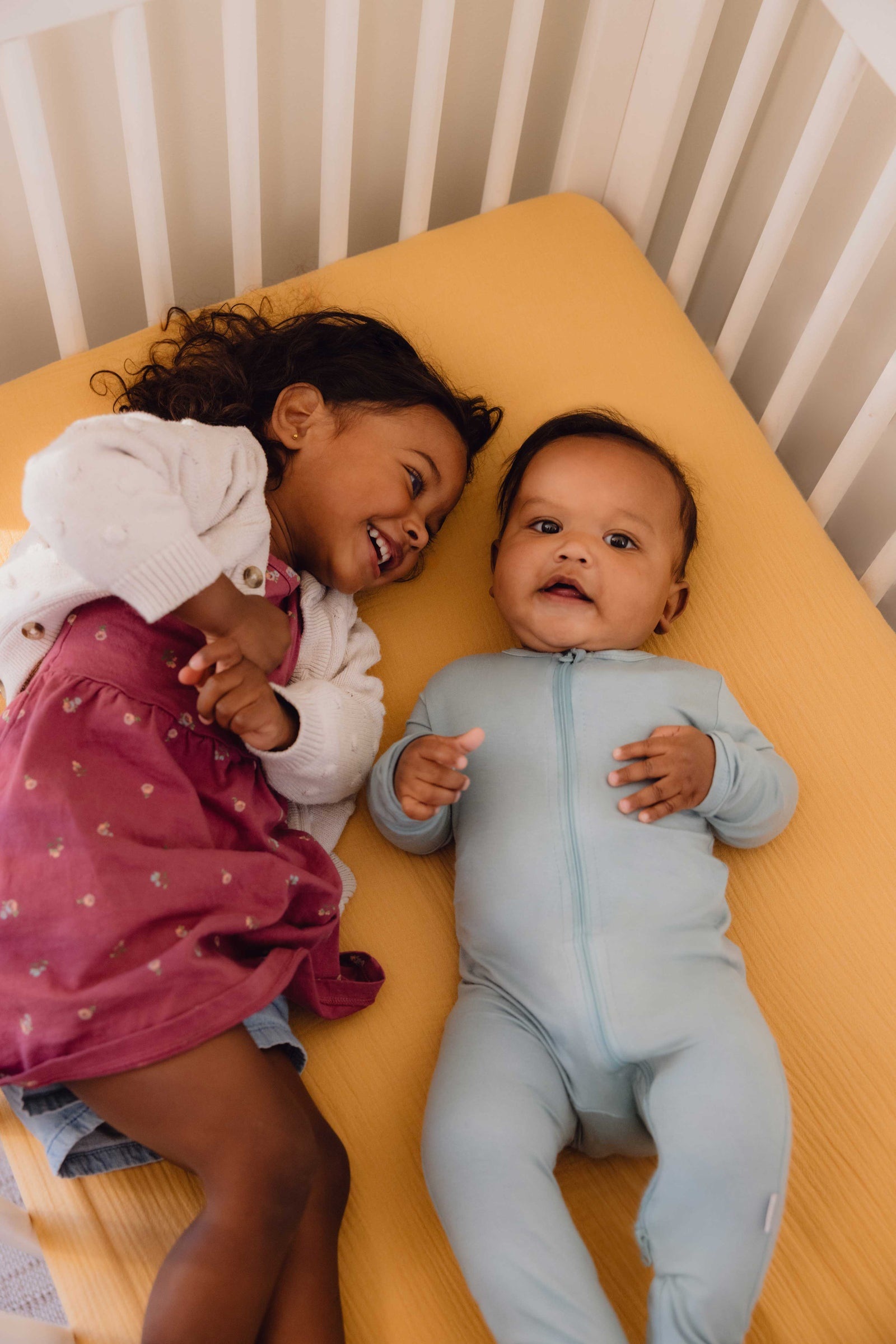 Two children smiling together in a crib during a Nanit lifestyle photo shoot