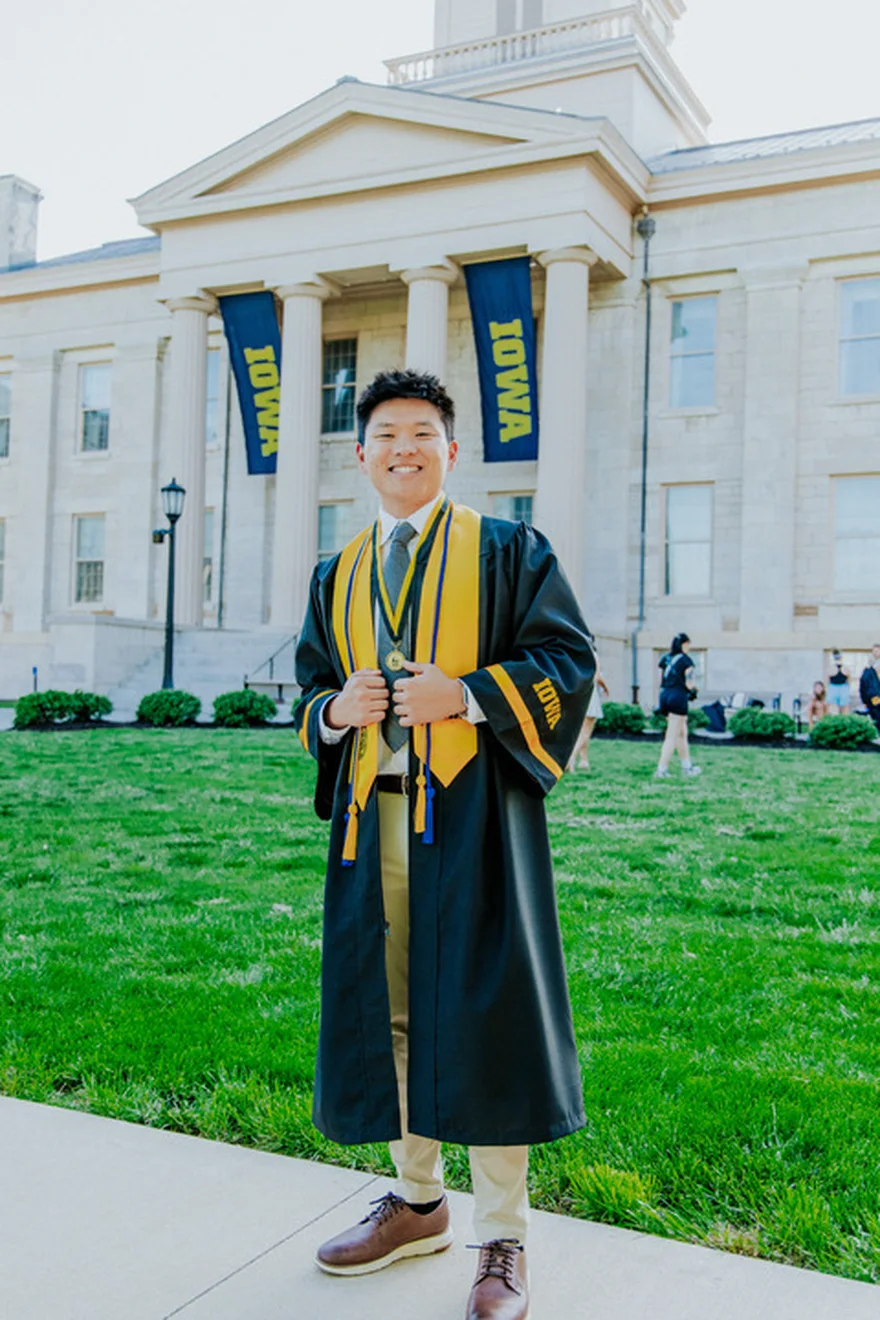 Nate Herkelman in cap and gown outside the Old Capitol at the University of Iowa