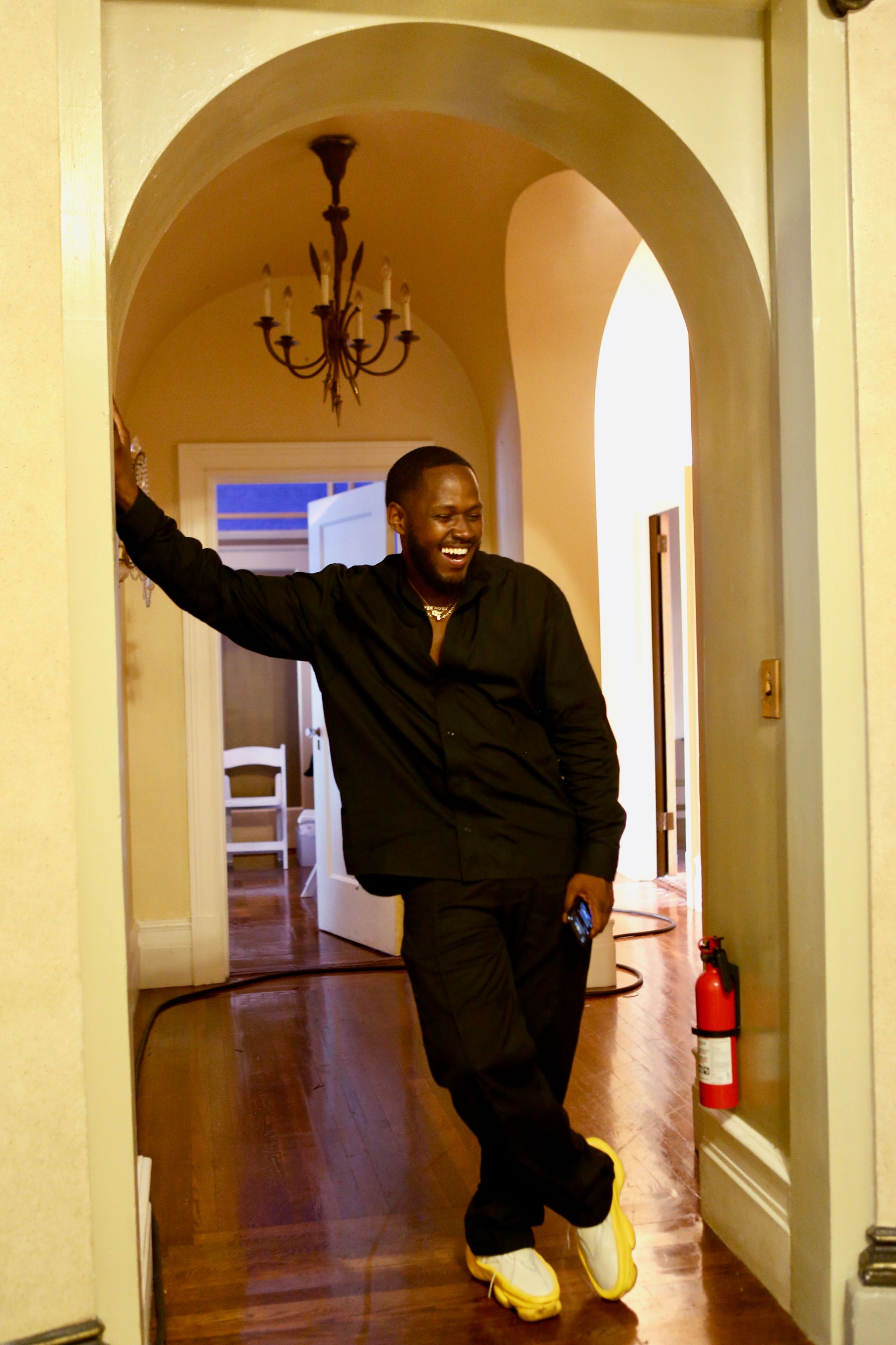 Nate Hinton laughing in a doorway, wearing black with yellow-accented shoes