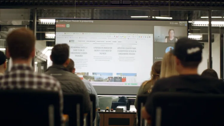 Monumetric colleagues seated in a meeting facing a presentation screen