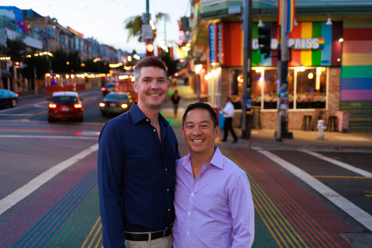 Nate Smith, left, and his husband Chris Cheng standing together on a rainbow-striped street in San Francisco