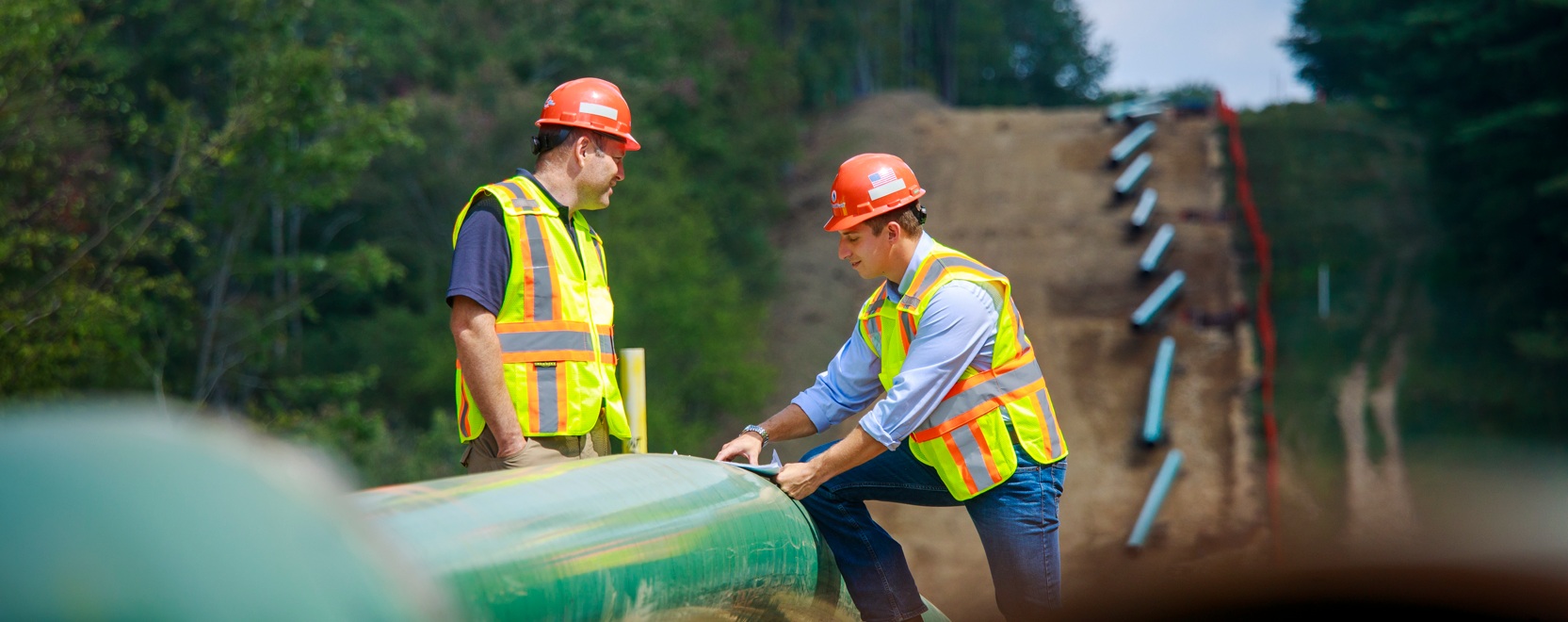 Two workers in orange hard hats examining a pipeline at a National Fuel FM100 construction site