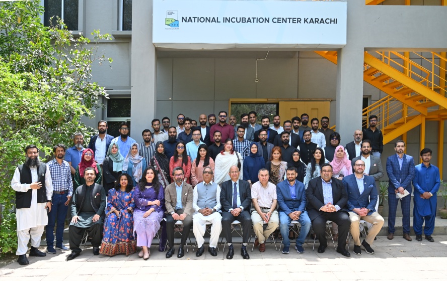 NIC Karachi cohort gathering outside the center, beside trees and a yellow staircase