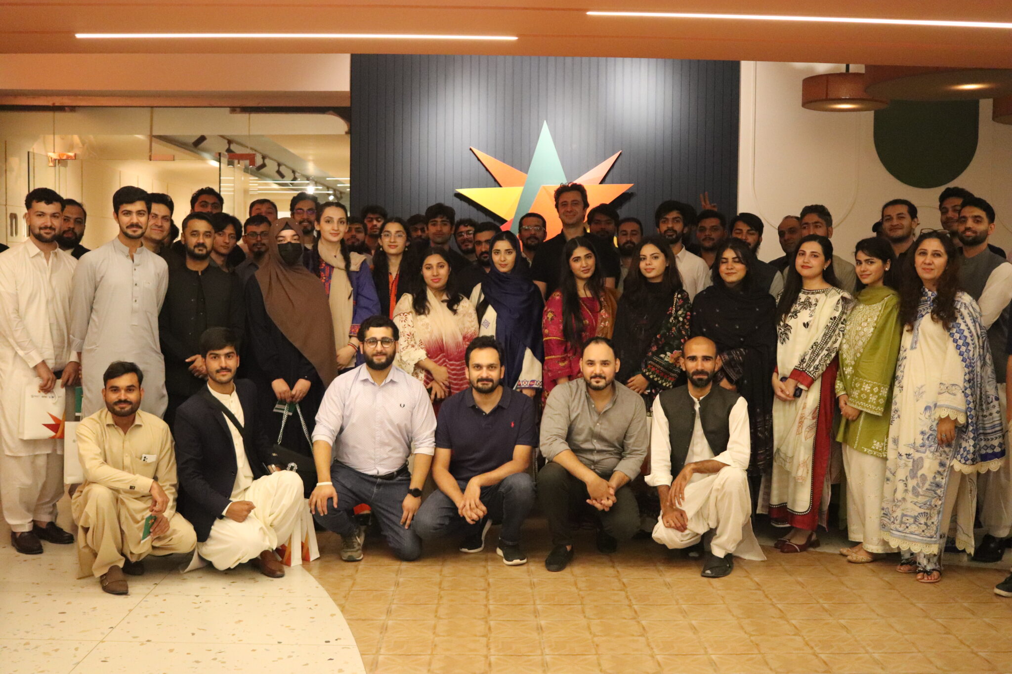 A group gathered inside NIC Peshawar beneath its colorful wall emblem