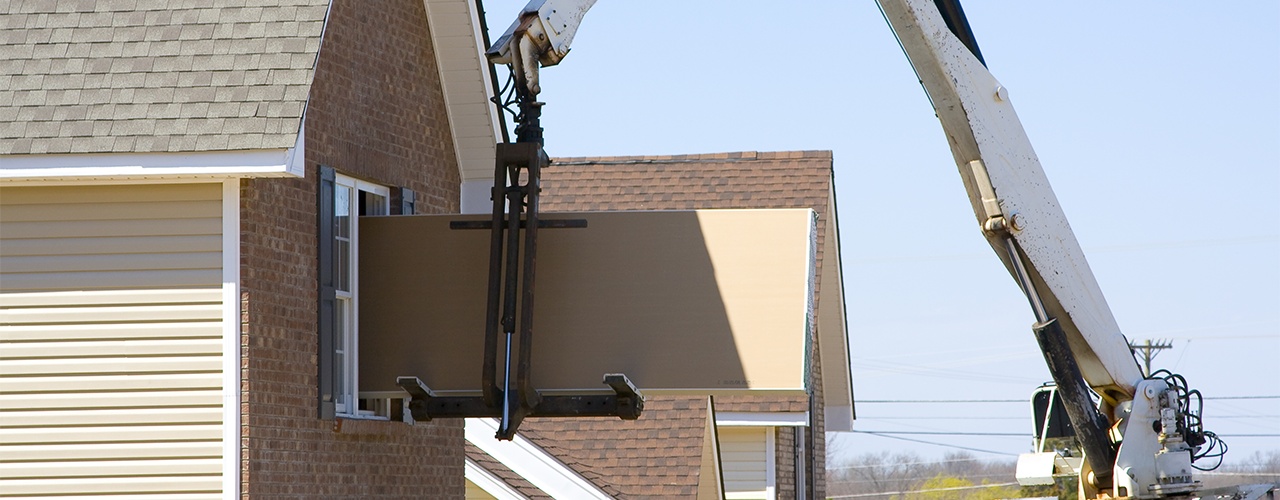Boom trucks placing drywall through upper-floor openings of a building under construction