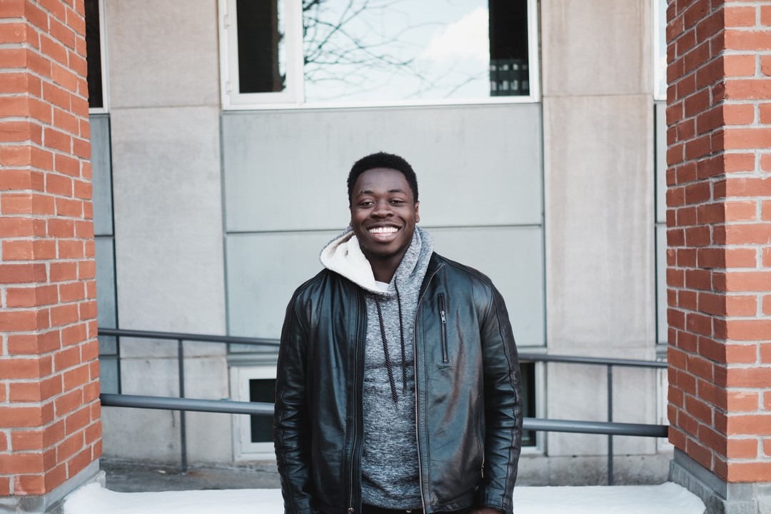 Natu Myers smiling outdoors between brick pillars in the photograph accompanying his 2016 essay