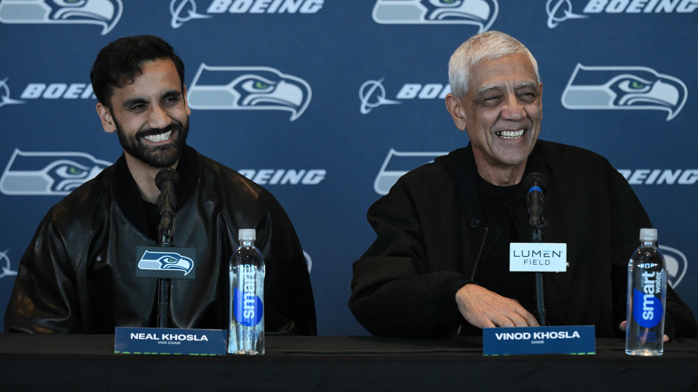 Neal Khosla, left, and his father Vinod smiling at microphones during the September 2026 Seahawks press conference.
